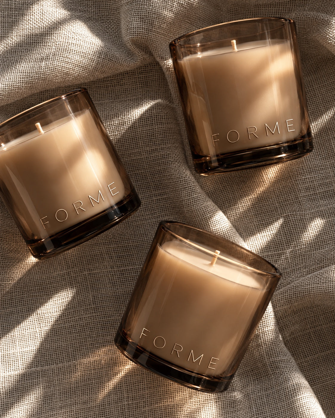 Three FORME 8 oz candles on textured linen